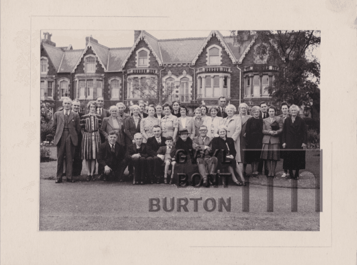 Black and white photo of a large group of people in front of a terrace of buildings