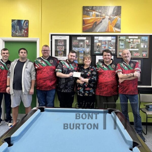 A group of people stand by a pool table handing over a cheque